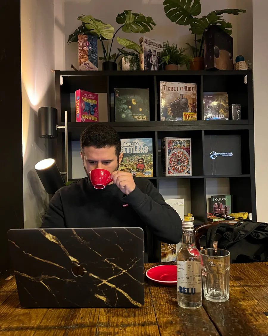 Lucas having a coffee at a wooden table with a laptop